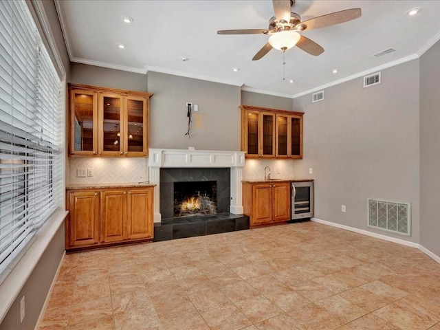 unfurnished living room with ceiling fan, a fireplace, beverage cooler, and ornamental molding