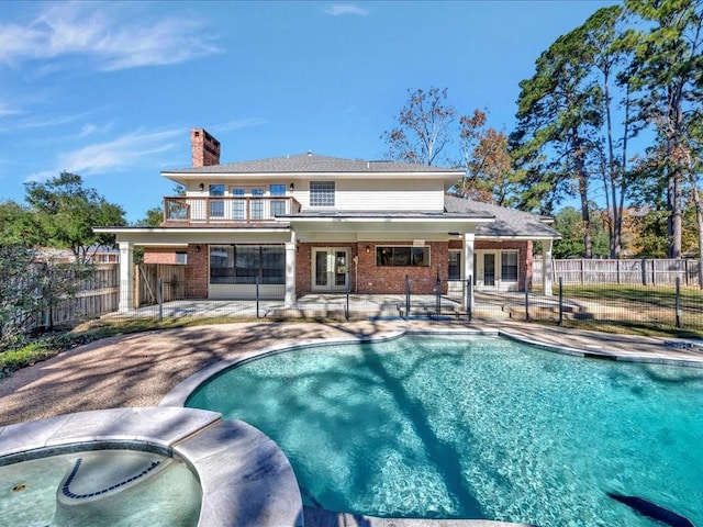 exterior space featuring a patio area, a swimming pool with hot tub, french doors, and a balcony