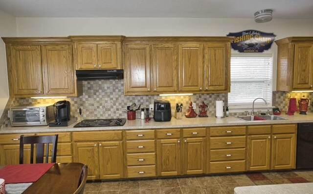 kitchen featuring brown cabinets, light countertops, a sink, under cabinet range hood, and black appliances