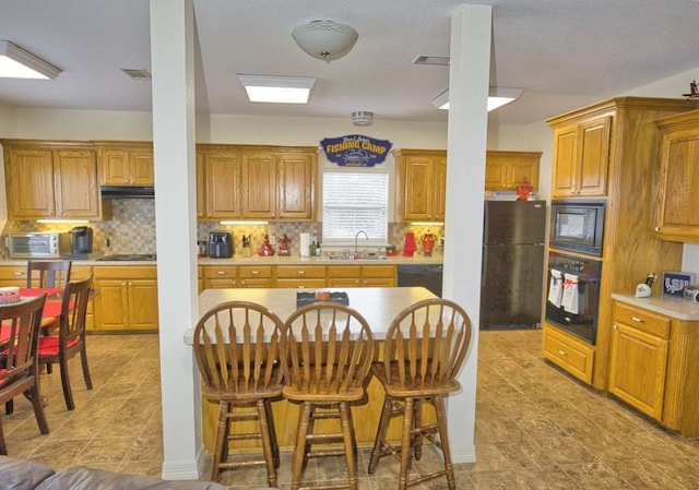 kitchen with a kitchen bar, sink, backsplash, and black appliances