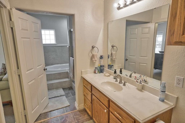 full bath with a tub to relax in, a textured wall, and vanity