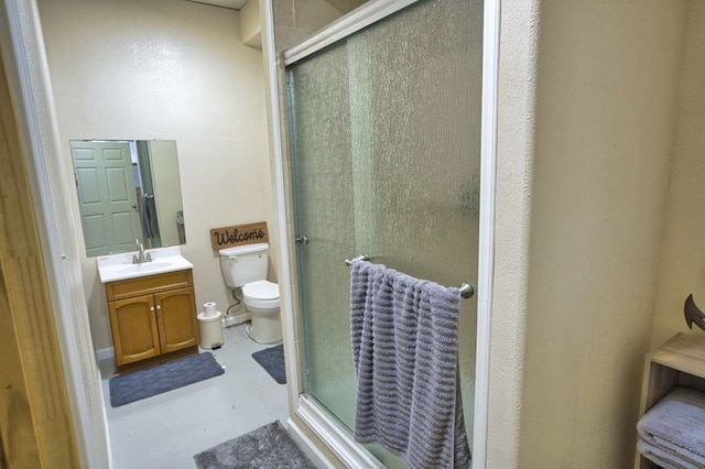 bathroom featuring vanity, toilet, concrete flooring, and a shower with door