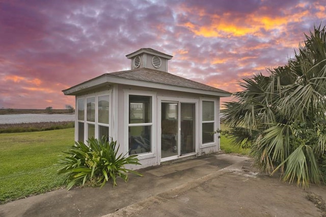 property exterior at dusk featuring an outbuilding, a water view, and a yard