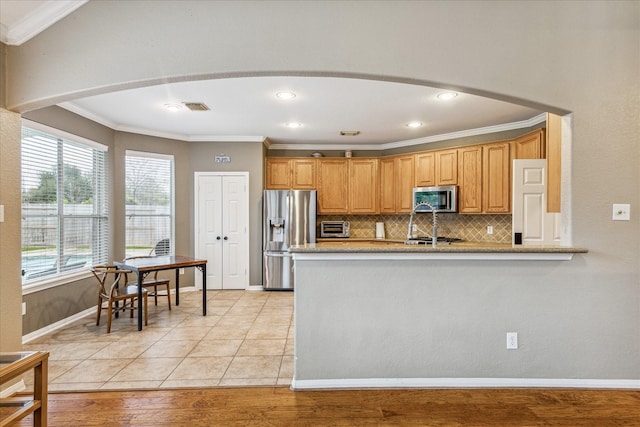 kitchen with light stone countertops, crown molding, decorative backsplash, appliances with stainless steel finishes, and light wood-type flooring