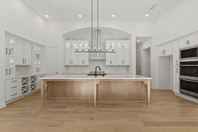 kitchen with a spacious island, white cabinetry, decorative light fixtures, and light hardwood / wood-style flooring