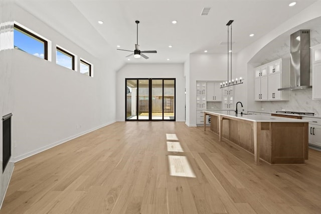 kitchen featuring pendant lighting, white cabinetry, decorative backsplash, wall chimney exhaust hood, and a spacious island