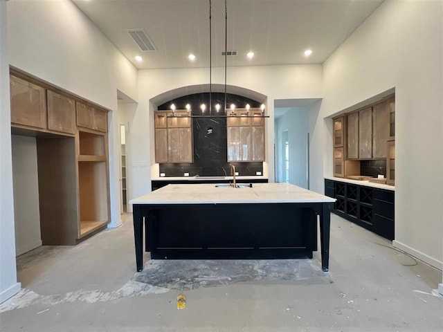 kitchen featuring decorative backsplash, sink, pendant lighting, and a kitchen island with sink