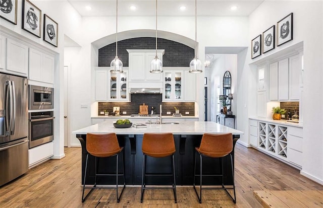 kitchen featuring stainless steel appliances, a kitchen island with sink, decorative light fixtures, white cabinets, and sink