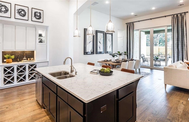 kitchen with light stone countertops, decorative backsplash, sink, hanging light fixtures, and stainless steel dishwasher