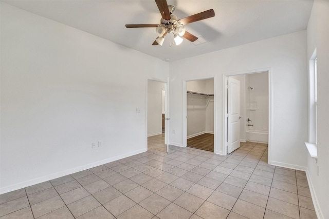 unfurnished bedroom with ensuite bathroom, ceiling fan, a spacious closet, light tile patterned floors, and a closet