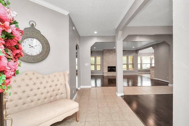 foyer featuring a stone fireplace, ornamental molding, a textured ceiling, and light hardwood / wood-style flooring