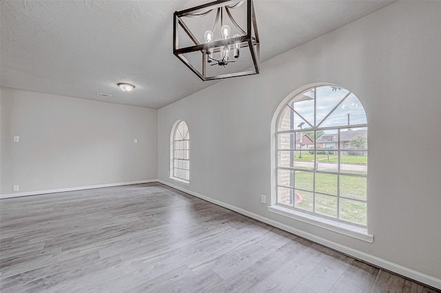 empty room featuring wood-type flooring, an inviting chandelier, and a wealth of natural light