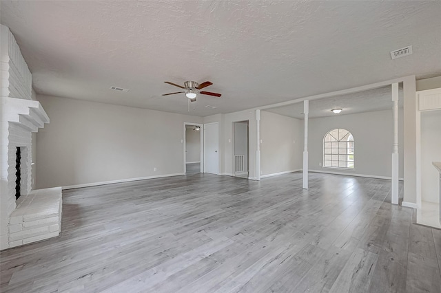 unfurnished living room with ceiling fan, light wood-type flooring, a textured ceiling, and a brick fireplace