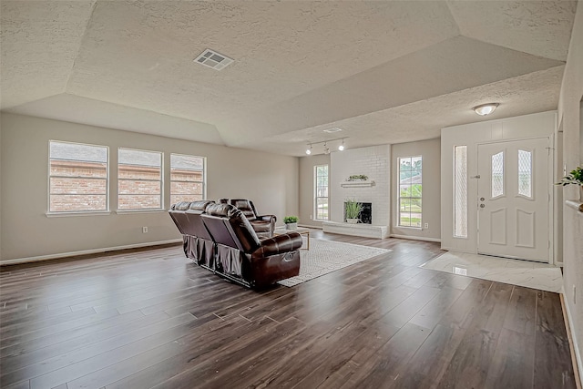 living room featuring vaulted ceiling, a brick fireplace, and dark wood-type flooring