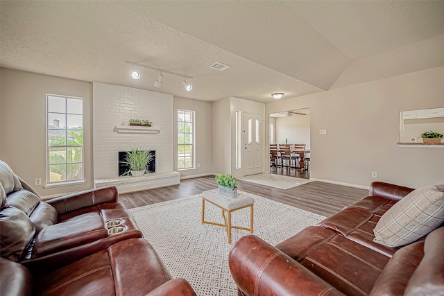 living room featuring ceiling fan, a textured ceiling, vaulted ceiling, a fireplace, and hardwood / wood-style flooring