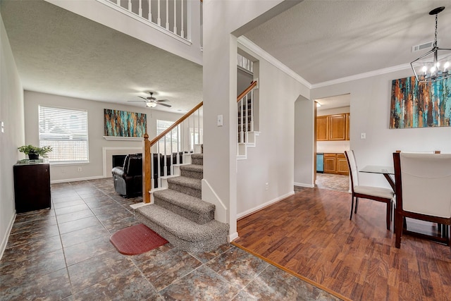 entrance foyer with a textured ceiling, ceiling fan with notable chandelier, crown molding, and dark wood-type flooring