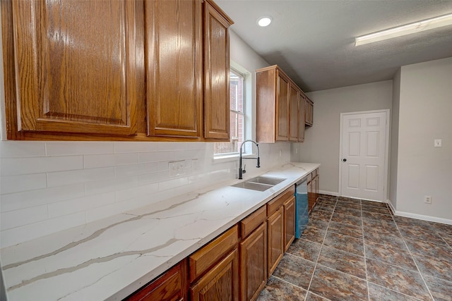 kitchen featuring decorative backsplash, dishwasher, sink, and light stone counters