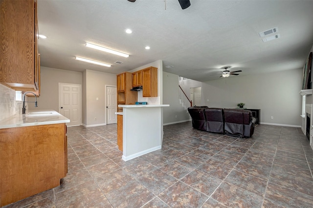 kitchen with kitchen peninsula, a fireplace, ceiling fan, and sink