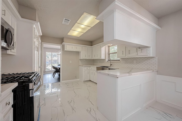 kitchen featuring decorative backsplash, appliances with stainless steel finishes, light stone countertops, sink, and white cabinetry