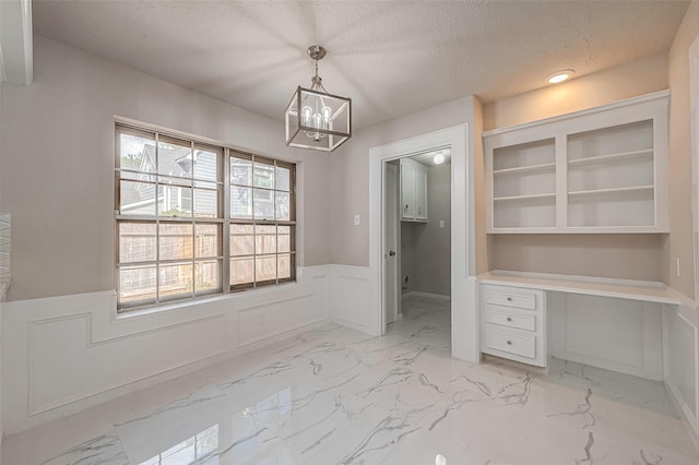 interior space with a textured ceiling, an inviting chandelier, built in features, and built in desk