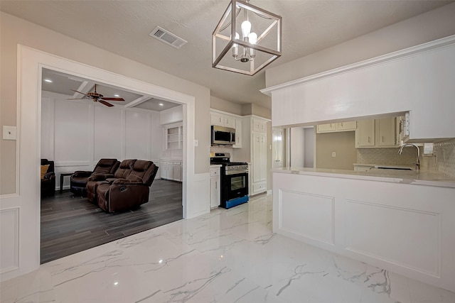 kitchen with stove, sink, decorative light fixtures, light hardwood / wood-style flooring, and white cabinetry