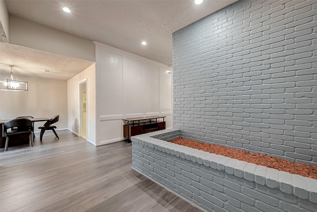 interior space with hardwood / wood-style flooring, a textured ceiling, brick wall, and an inviting chandelier