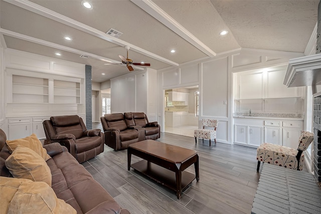 living room with ceiling fan, built in features, wood-type flooring, a textured ceiling, and vaulted ceiling