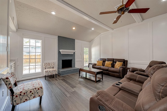 living room with a textured ceiling, ceiling fan, wood-type flooring, lofted ceiling with beams, and a fireplace