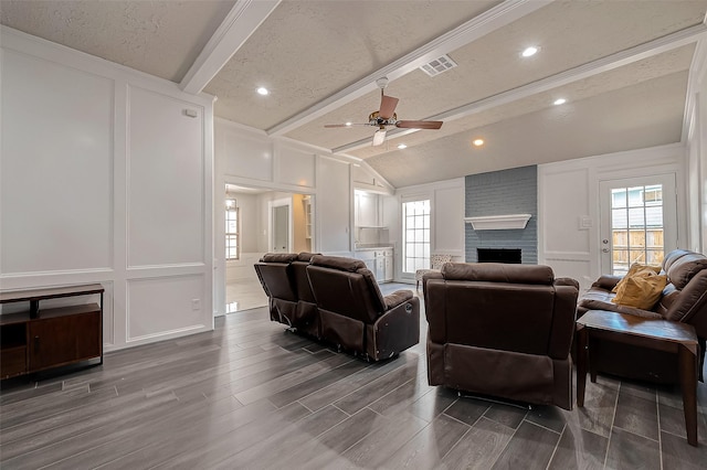 living room with a brick fireplace, a textured ceiling, ceiling fan, lofted ceiling with beams, and dark hardwood / wood-style floors