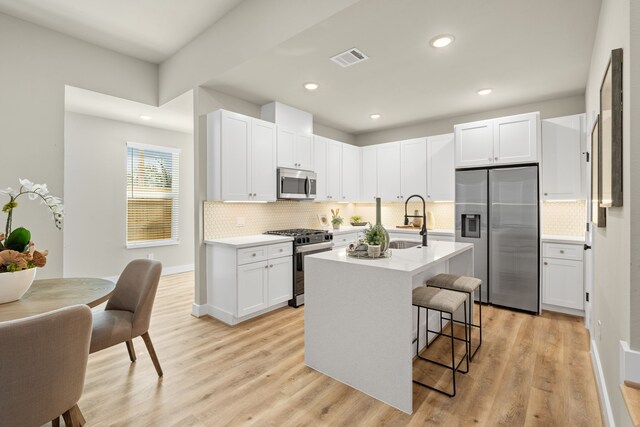 kitchen with a breakfast bar area, white cabinetry, stainless steel appliances, light hardwood / wood-style floors, and a center island with sink