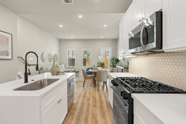 kitchen featuring sink, stainless steel appliances, light hardwood / wood-style floors, white cabinets, and decorative backsplash