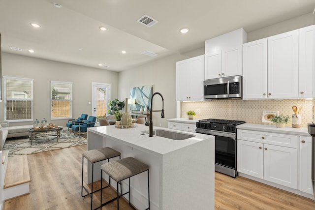 kitchen with sink, appliances with stainless steel finishes, an island with sink, white cabinets, and decorative backsplash