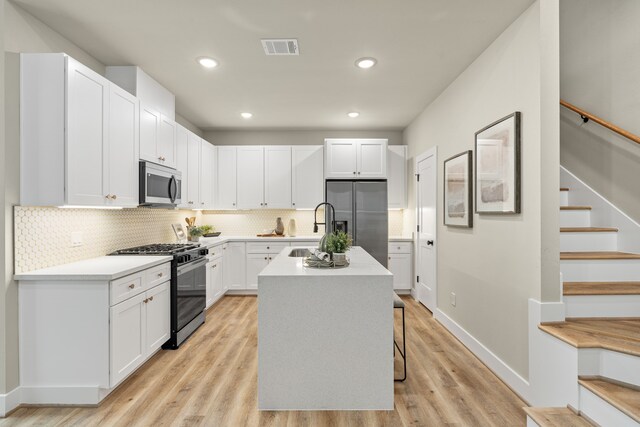 kitchen featuring sink, appliances with stainless steel finishes, an island with sink, white cabinets, and a kitchen bar