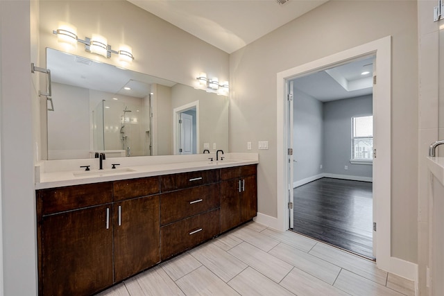 bathroom with double vanity, a stall shower, a sink, and baseboards