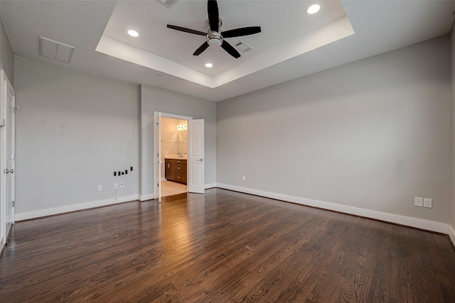 unfurnished bedroom featuring baseboards, visible vents, dark wood-style flooring, a tray ceiling, and recessed lighting