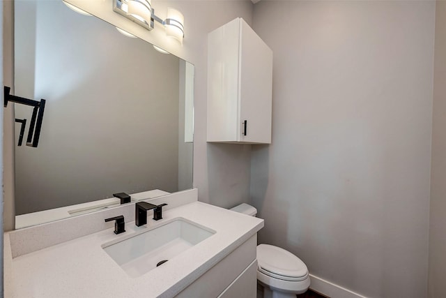 half bathroom featuring toilet, baseboards, and vanity