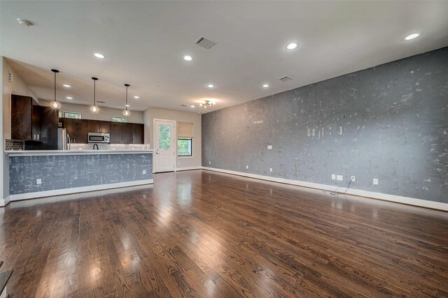 kitchen featuring kitchen peninsula, appliances with stainless steel finishes, dark brown cabinetry, dark wood-type flooring, and pendant lighting