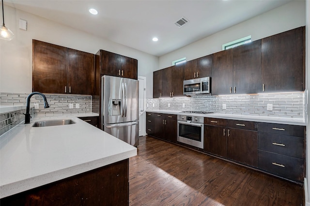 kitchen with appliances with stainless steel finishes, dark wood-style flooring, a sink, and dark brown cabinetry