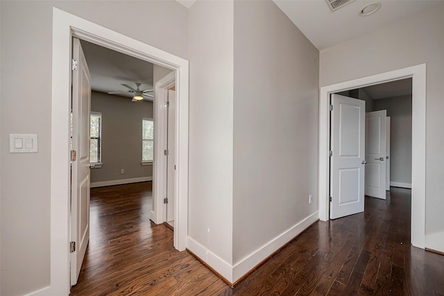 hallway with visible vents, baseboards, and dark wood-type flooring