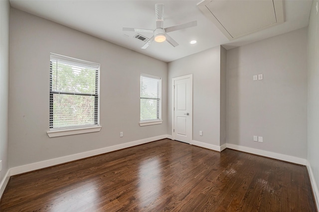 spare room featuring visible vents, dark wood-type flooring, attic access, a ceiling fan, and baseboards