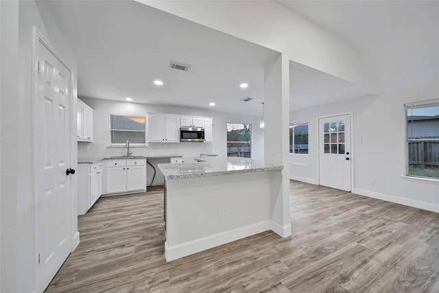 kitchen with white cabinets, light stone counters, appliances with stainless steel finishes, and light hardwood / wood-style flooring