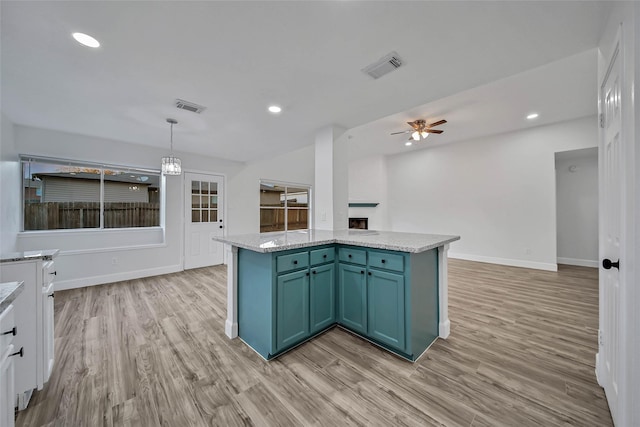 kitchen with decorative light fixtures, a kitchen island, light wood-type flooring, and ceiling fan