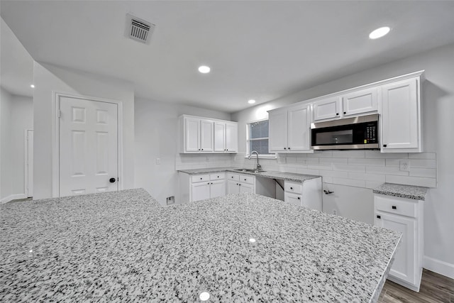 kitchen with white cabinetry, stainless steel appliances, light stone counters, backsplash, and hardwood / wood-style floors