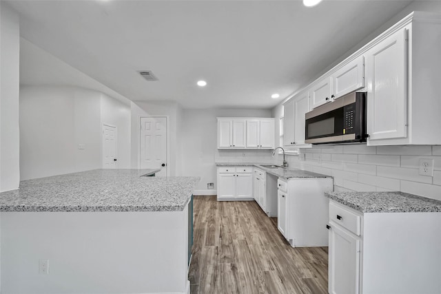 kitchen with tasteful backsplash, stainless steel appliances, sink, light hardwood / wood-style floors, and white cabinetry