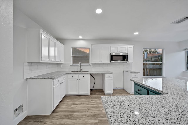 kitchen with white cabinets, light wood-type flooring, light stone counters, and sink