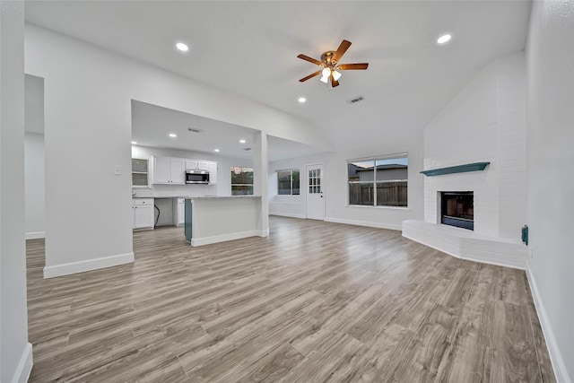 unfurnished living room with ceiling fan, light hardwood / wood-style flooring, lofted ceiling, and a brick fireplace