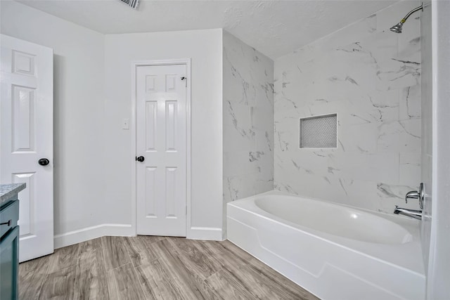 bathroom with a textured ceiling, vanity, wood-type flooring, and tiled shower / bath combo