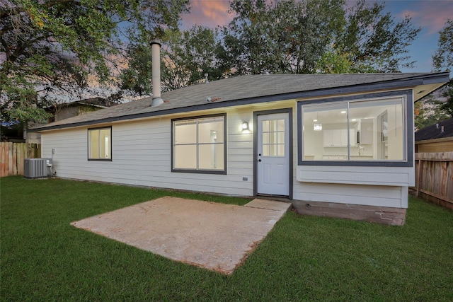 back house at dusk featuring a patio area, a yard, and cooling unit