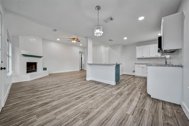 kitchen featuring white cabinets, ceiling fan with notable chandelier, hanging light fixtures, light wood-type flooring, and a fireplace