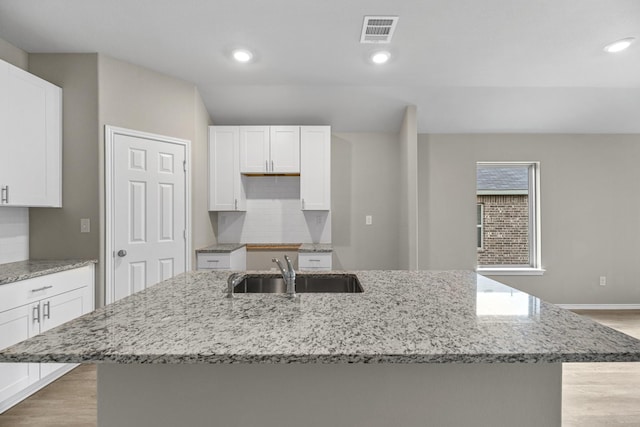 kitchen with light stone countertops, white cabinetry, a kitchen island with sink, and sink